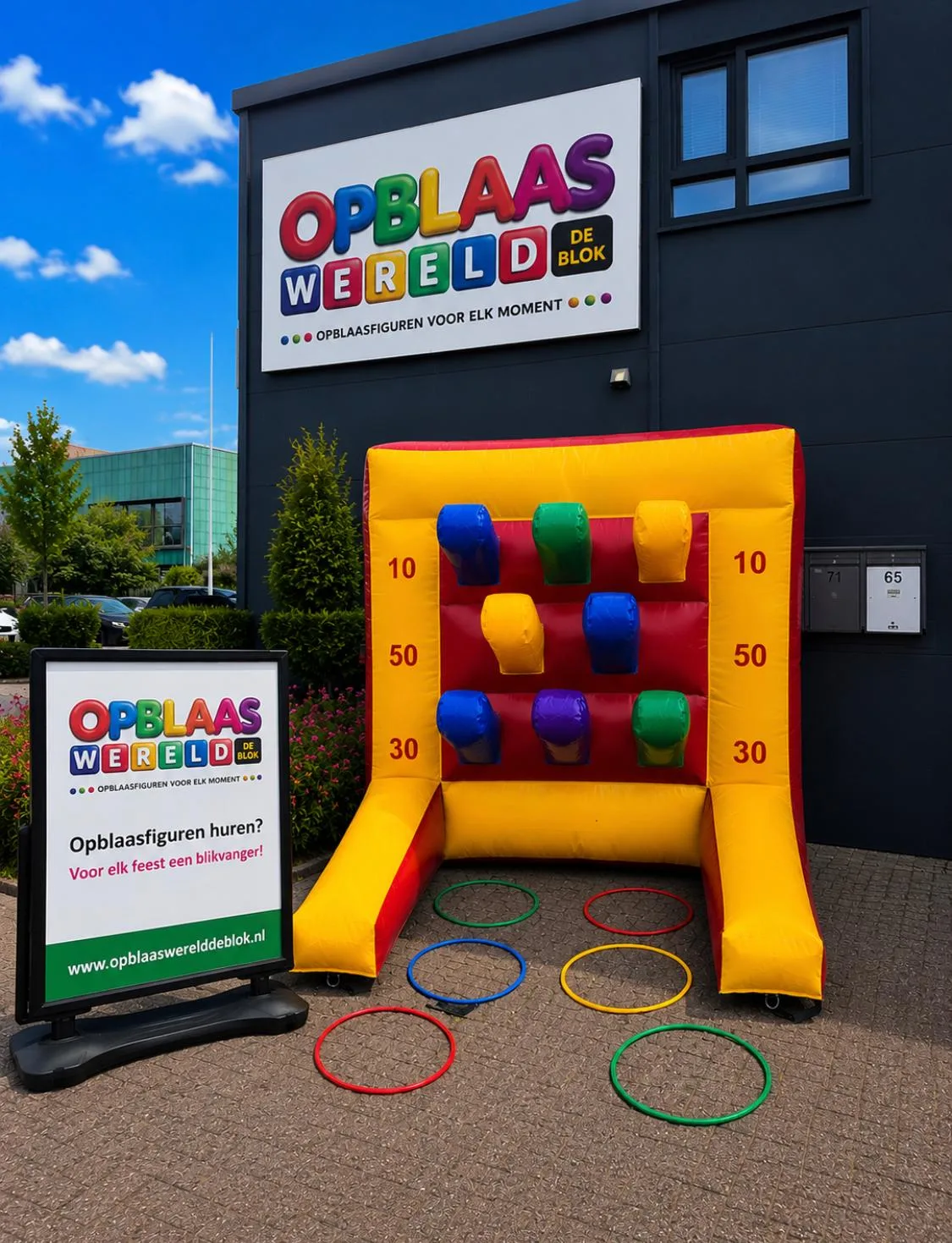 Geel-rood opblaasbaar ringwerpspel met gekleurde doelen en puntenwaardes 10, 30 en 50, met zes gekleurde ringen op de grond, voor het pand van Opblaaswereld de Blok.