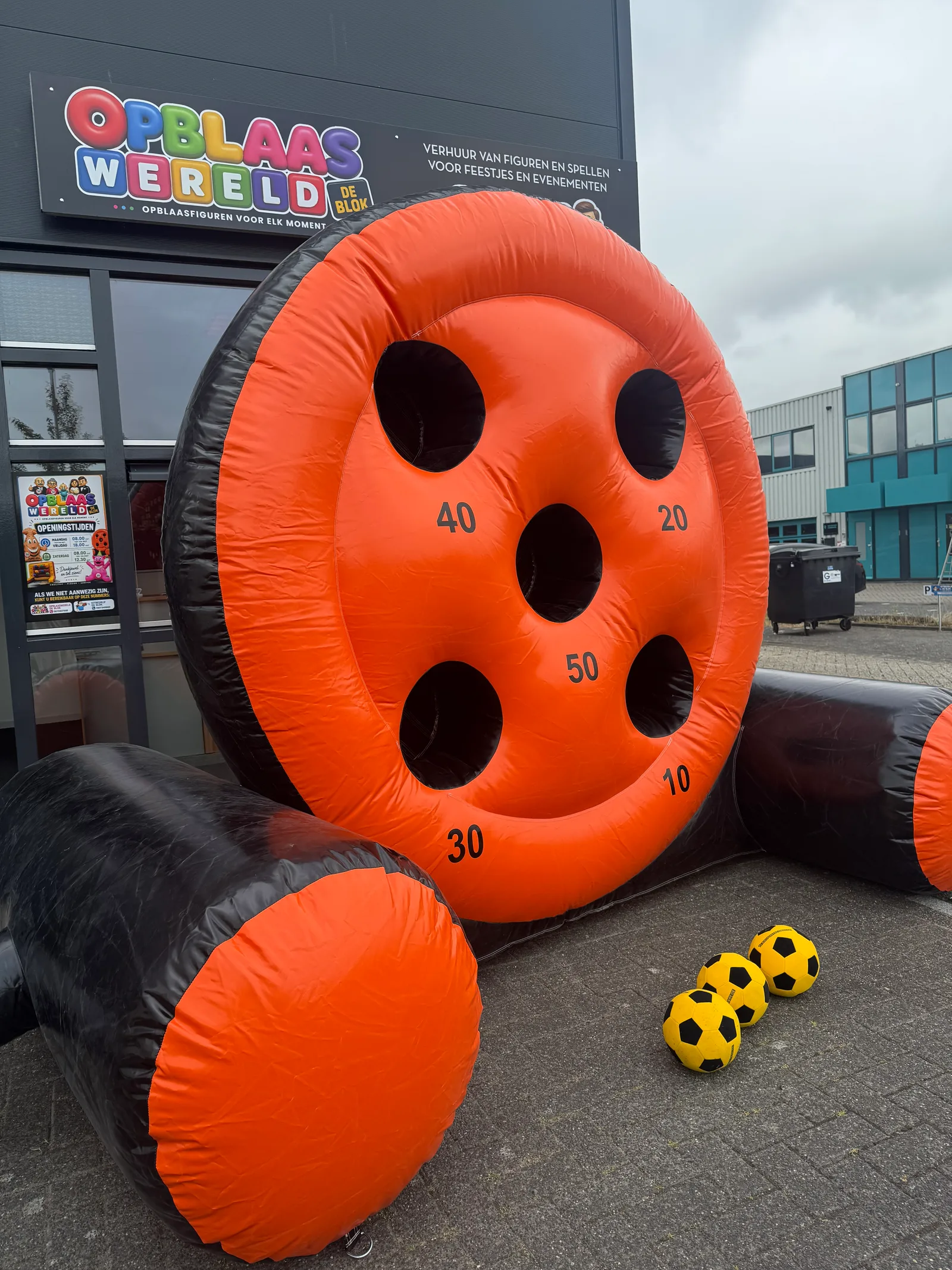 Oranje met zwarte opblaasbare Voetbal Schietschijf met vijf gaten en puntenaantallen 10, 20, 30, 40 en 50, staand voor het pand van Opblaaswereld de Blok.
