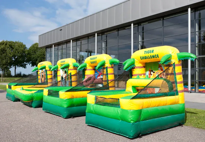 Vier opblaasbare junglespellen in groen en geel naast elkaar op straat voor een gebouw, met palmbomen en teksten als Tiger Challenge en Parrot Basket.