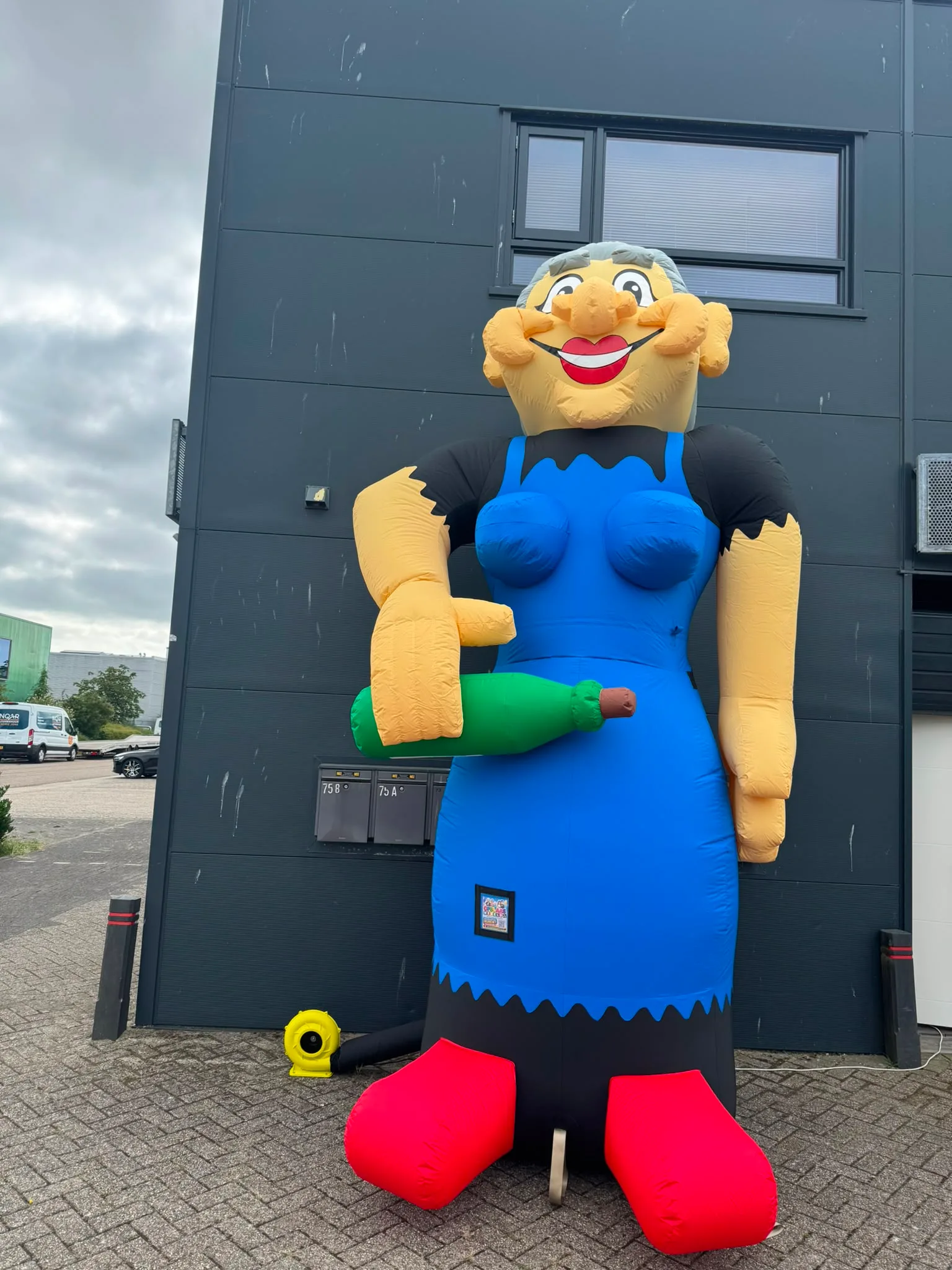 Opblaasbare Sarah van 4,3 meter met blauwe jurk, schort, grijs haar en rode voeten, opgesteld voor het pand van Opblaaswereld de Blok.