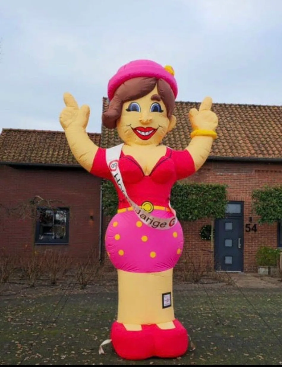 Opblaasbare Sarah dame van 3,8 meter in roze jurk met stippen en sjerp, duimen omhoog, opgesteld voor een woning.