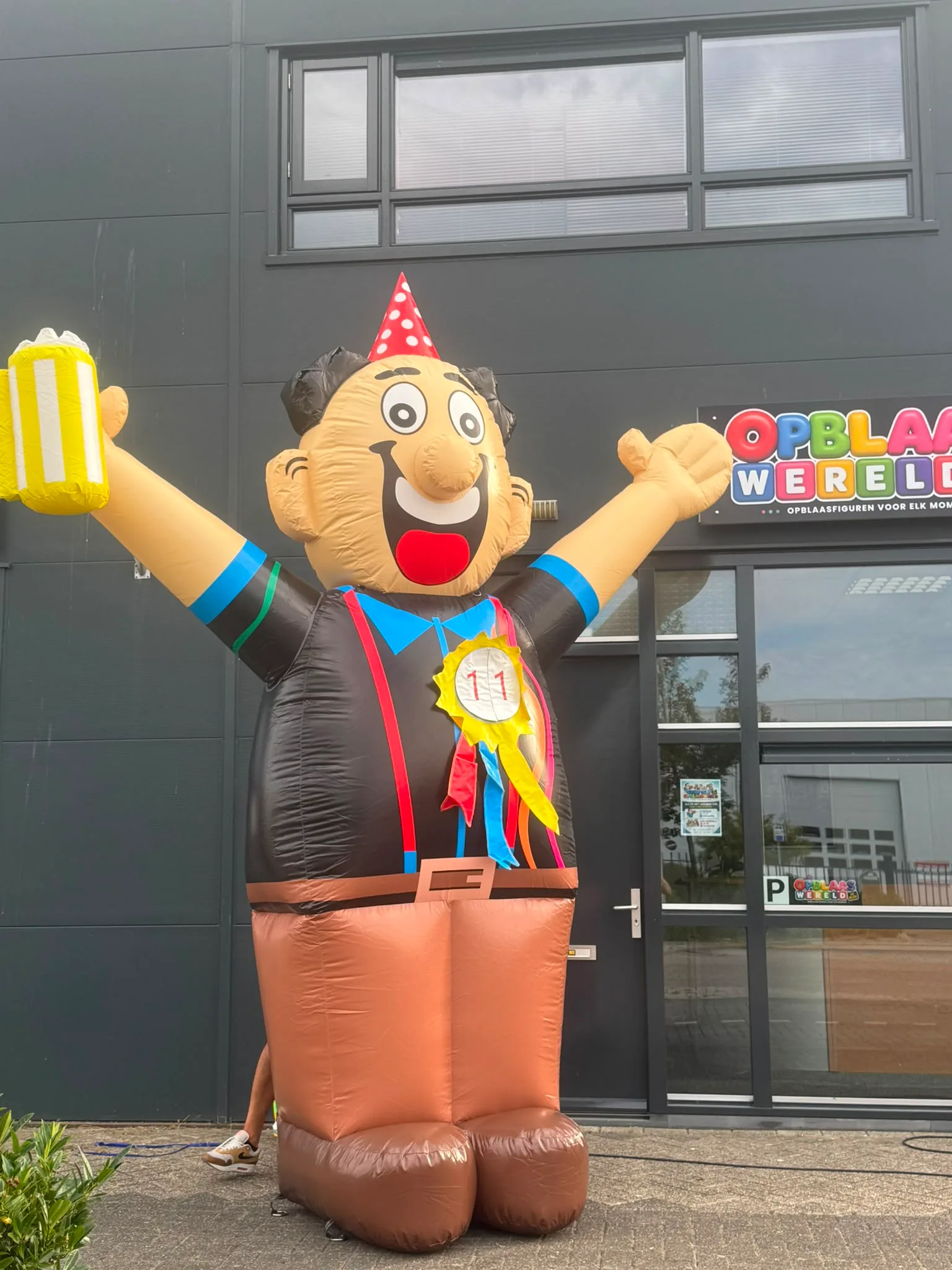 Grote opblaasbare feestpop Abraham met feestmuts, schuimend bierpul en rozet met het getal 50, staand voor het pand van Opblaaswereld.