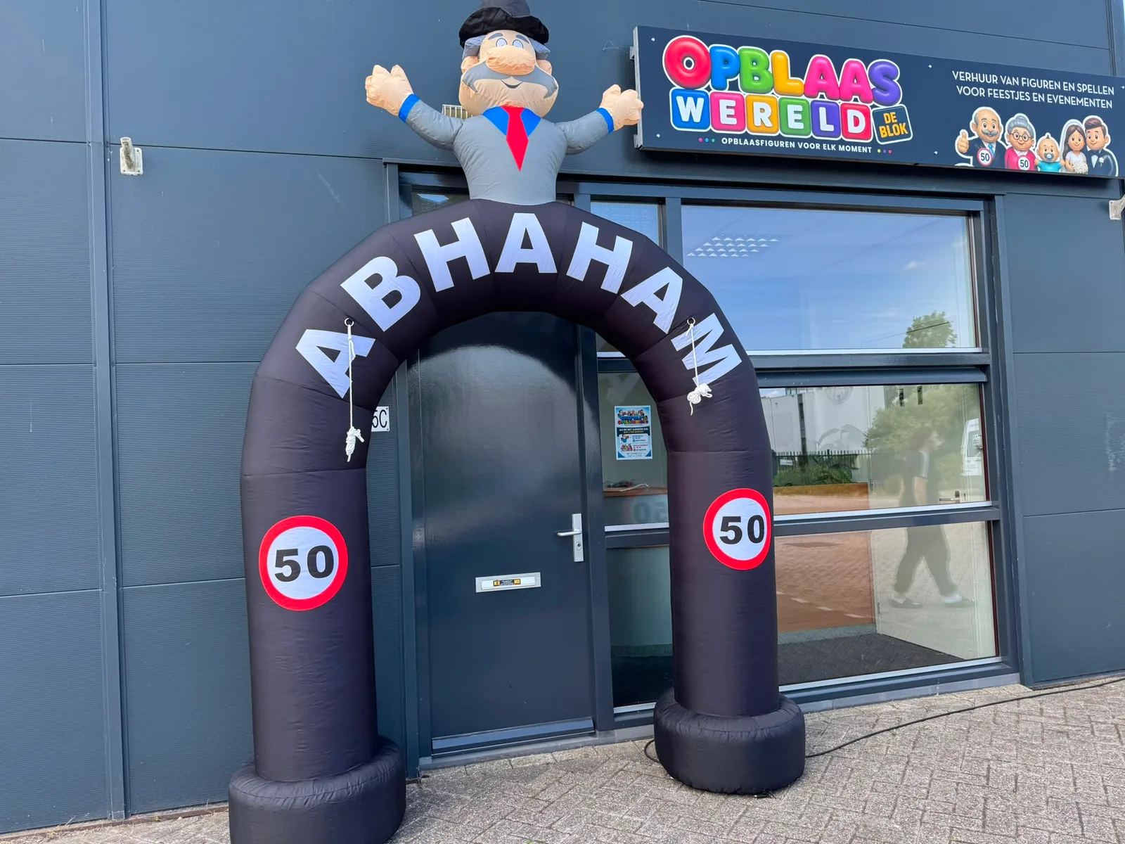 Zwarte opblaasboog met de tekst Abraham, twee borden met 50 en een opblaasfiguur van Abraham met hoge hoed erbovenop, opgesteld voor de ingang van Opblaaswereld de Blok.